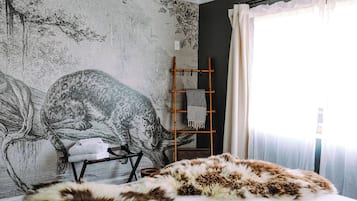 A bedroom with a large wall mural, a bed with a fur throw, a wooden ladder, and a chair.