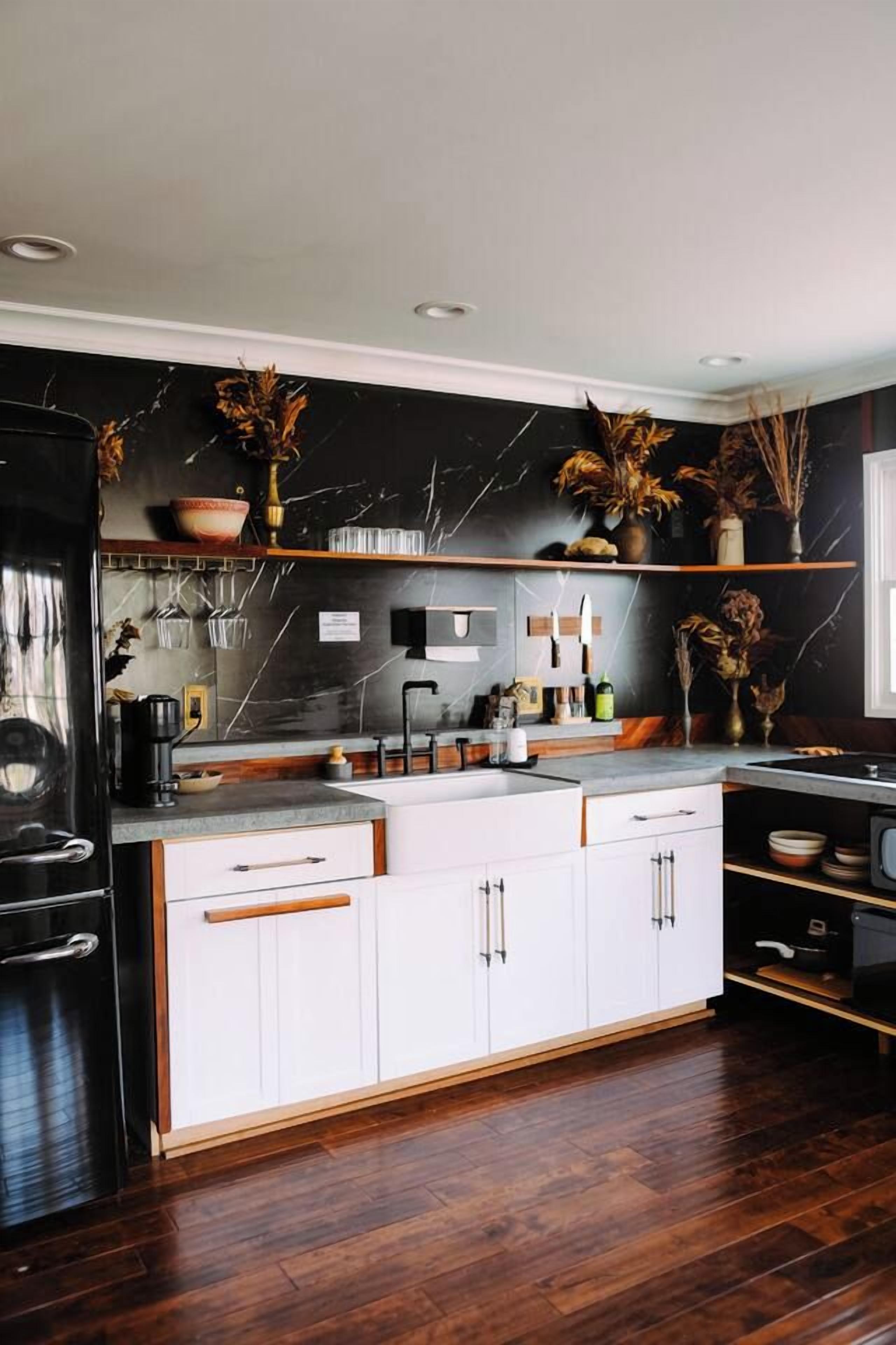 A modern kitchen with white cabinetry, a black marble backsplash, and wooden flooring.