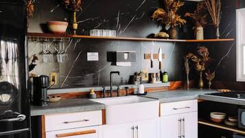 A modern kitchen with white cabinetry, a black marble backsplash, and wooden flooring.