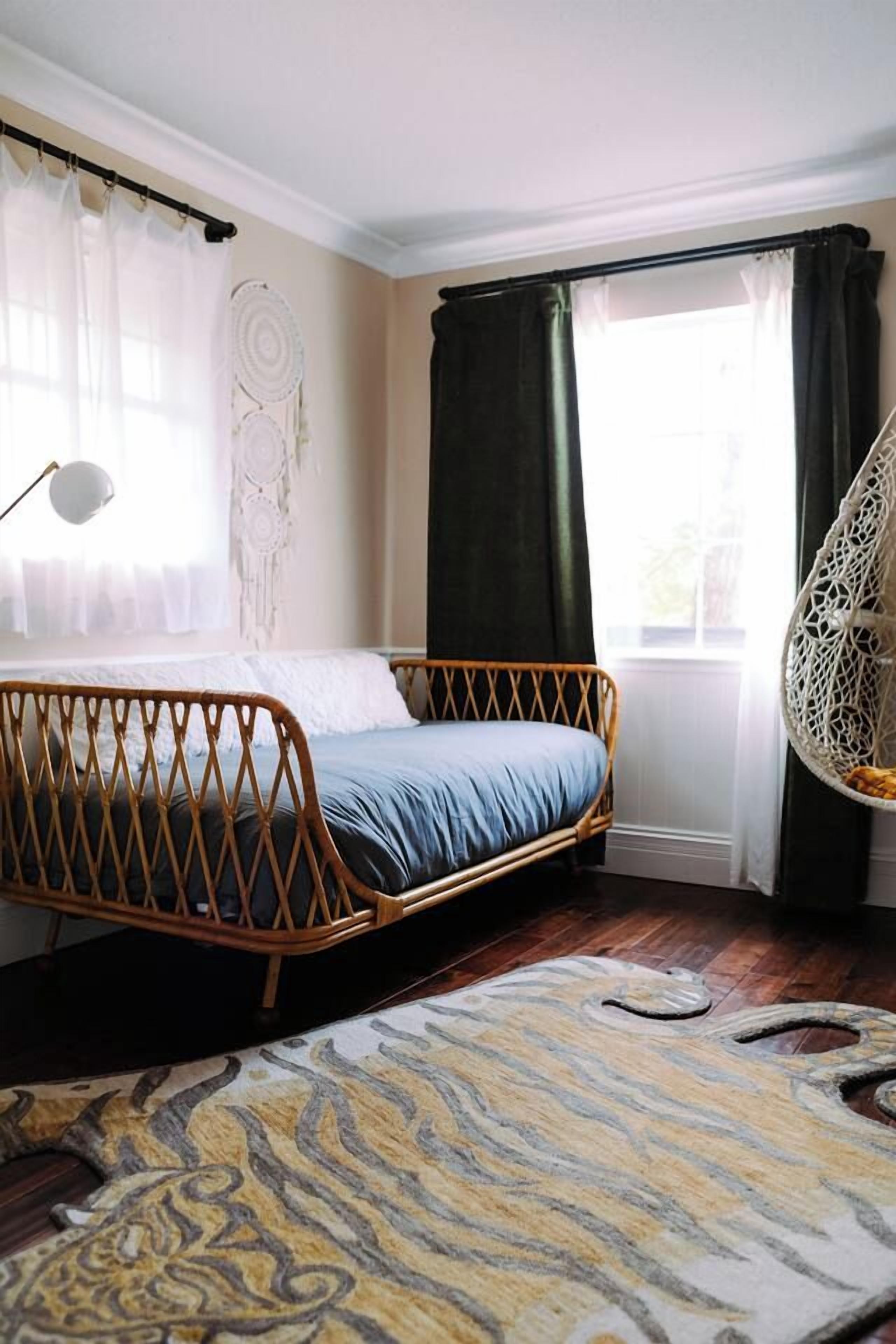 A room with a single bed, a hanging chair, a dreamcatcher, and a patterned rug.