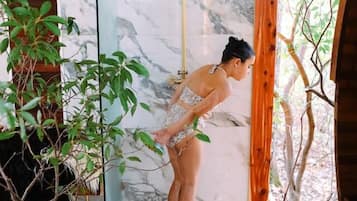A person in a bathroom with a marble wall, a shower, and a wooden floor.