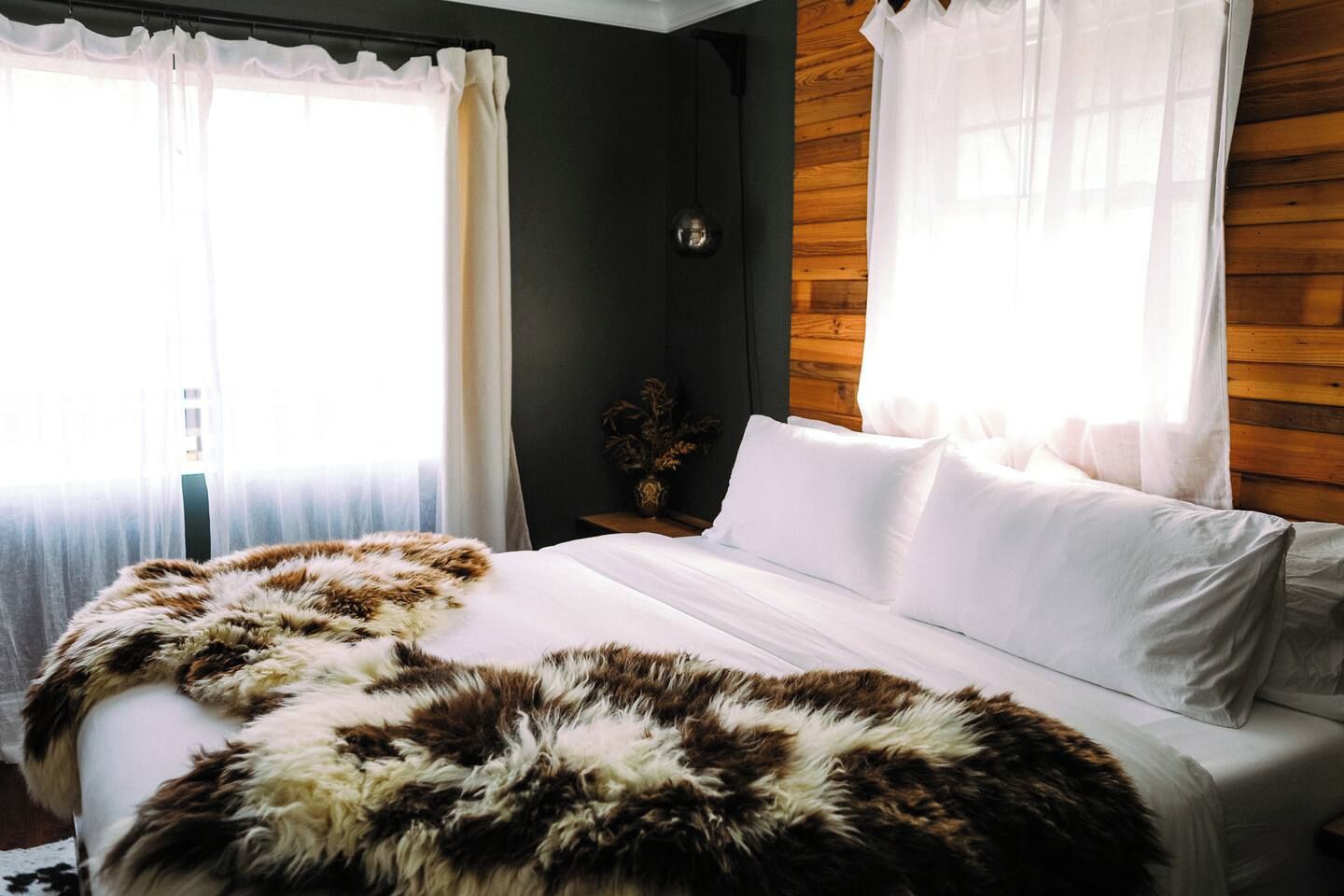 Une chambre à coucher avec un lit, du linge de lit blanc, un plaid en fourrure et des lambris en bois sur les murs.