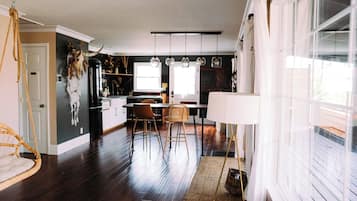 A modern kitchen with pendant lights, a dining area with chairs, and a large window with blinds.