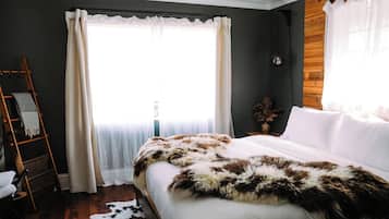 A bedroom with a bed, a ladder, a window with curtains, and a wooden wall.