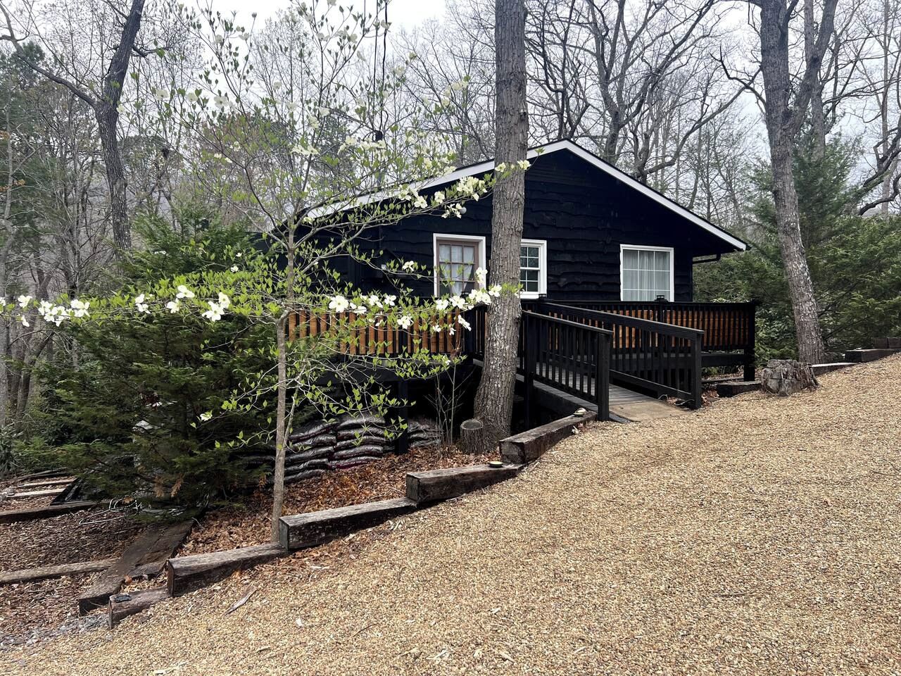 A cabin with a wooden deck, surrounded by trees and a garden area.