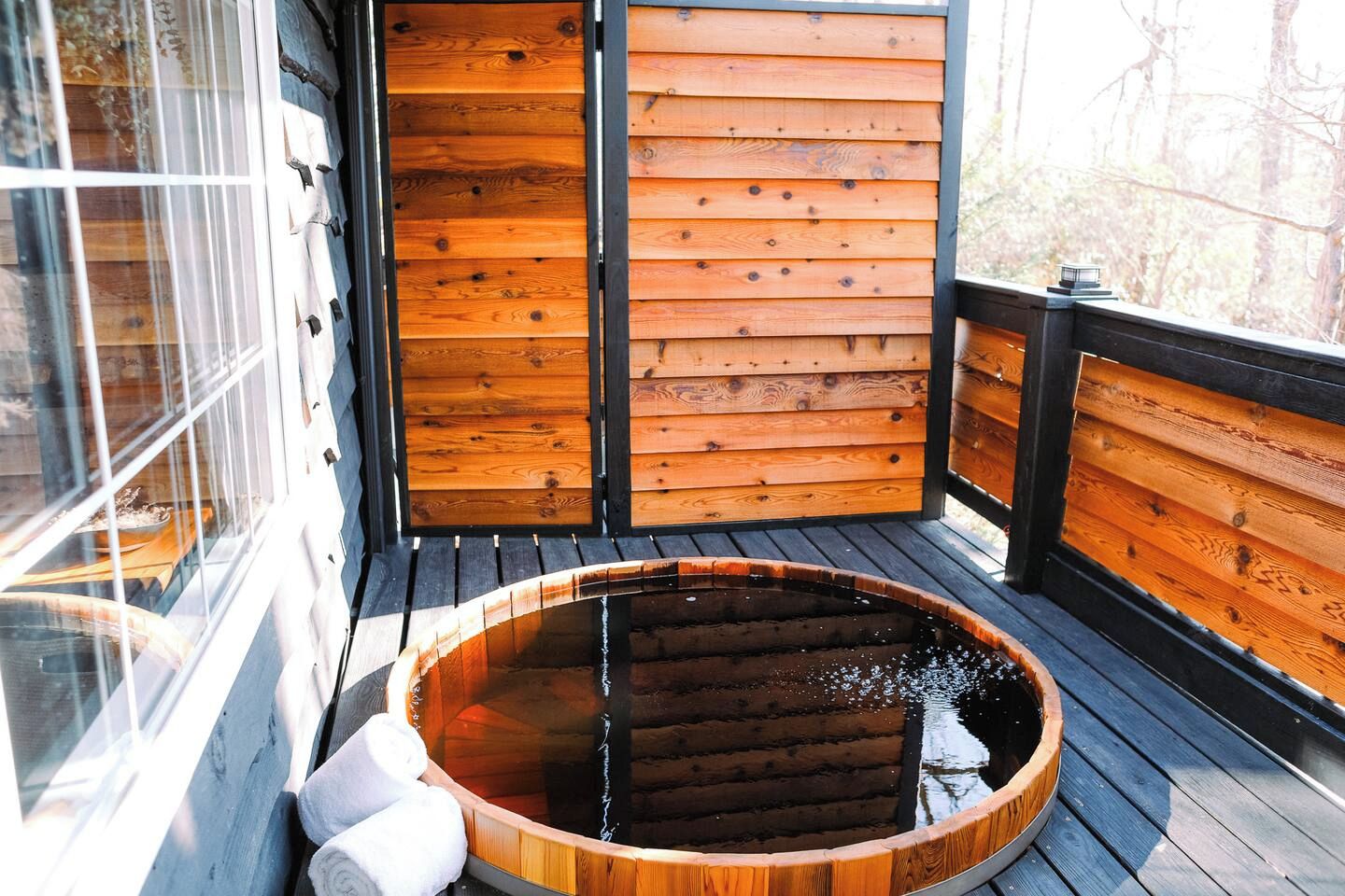 A wooden spa bath with a curved wooden edge, a wooden deck, and a glass door leading to a room.