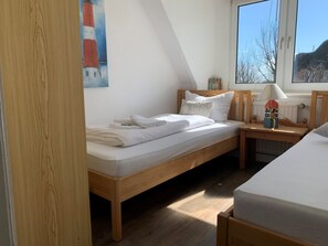 Un dormitorio con una cama individual, una mesita de noche con una lámpara y una ventana con vistas a un edificio.