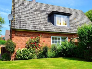 A two-story house with a sloped roof, a satellite dish, and a well-maintained garden with red flowers. - Jaardenhuug - OG (Utersum)