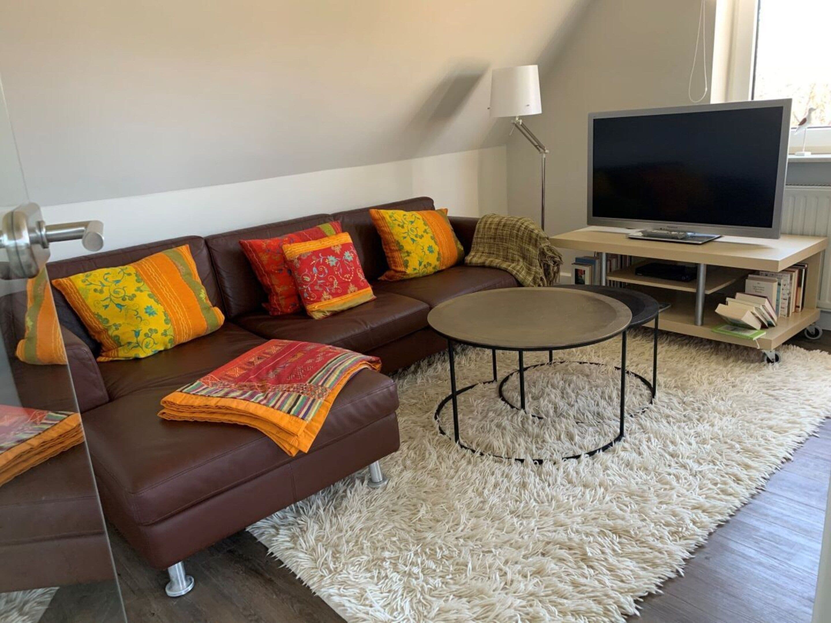 A modern living room with a brown leather sofa, a round coffee table, a flat-screen TV, and a white shag rug.