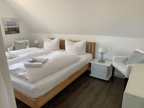 A hotel room with a double bed, two bedside tables, a chair, and a nightstand. - Jaardenhuug - OG (Utersum)