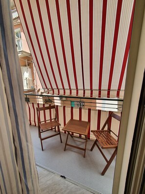 Un balcone con tende a righe, un tavolo in vetro e sedie di legno.