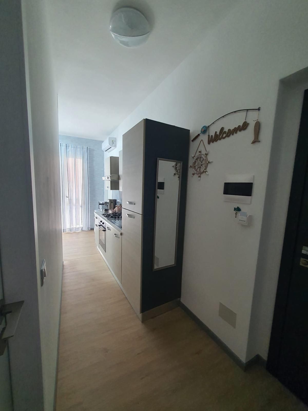 A hallway with a kitchen area, a door with a welcome sign, and a ceiling light fixture.