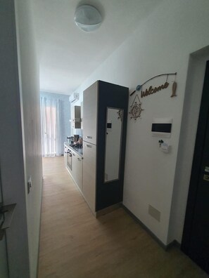 Un corridoio con angolo cottura, una porta con un cartello di benvenuto e una lampada a soffitto.