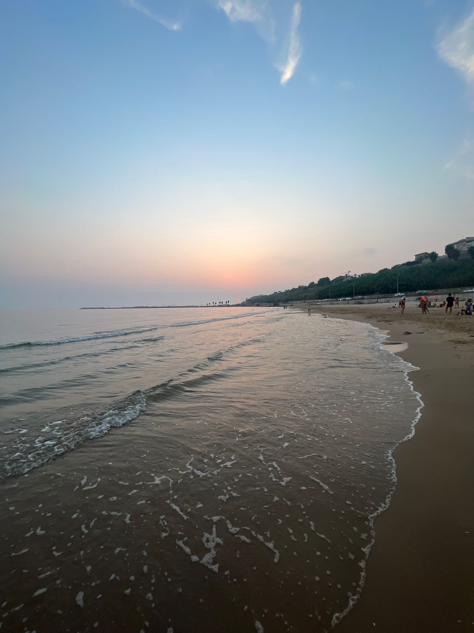 A beach with gentle waves, a clear sky, and a distant horizon.