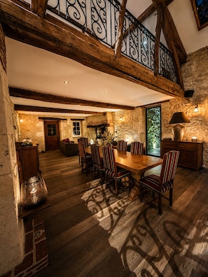 Un comedor amplio con una mesa y sillas de madera, una pared de piedra y un balcón con barandilla de hierro forjado.