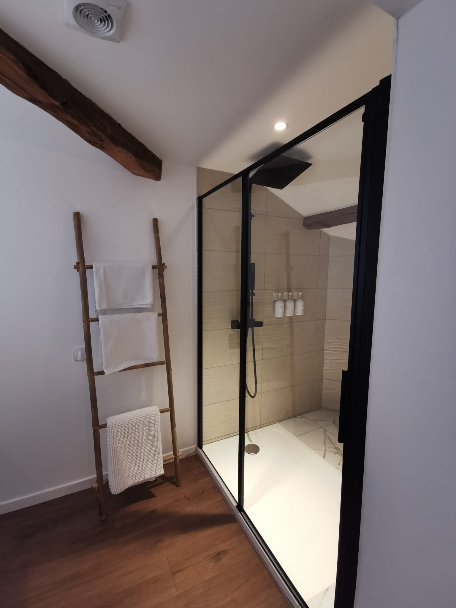Un baño moderno con cabina de ducha de vidrio, escalera de madera y un perchero.