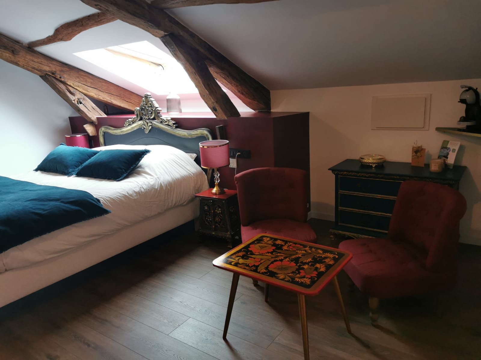 A bedroom with a bed, a red chair, a small table, a nightstand, and a dresser.