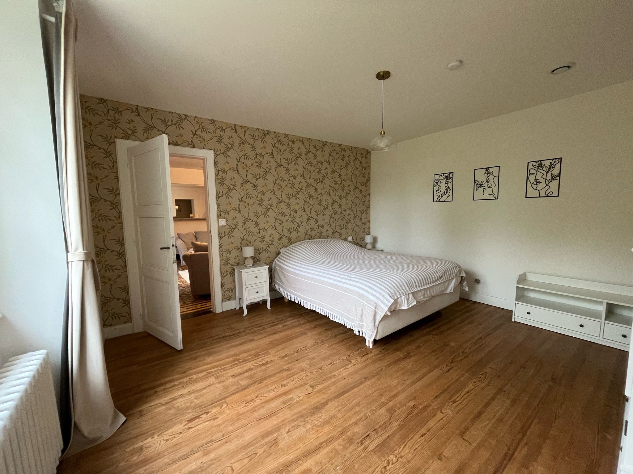 Un dormitorio con cama, mesita de noche, cómoda y una puerta que da a otra habitación.