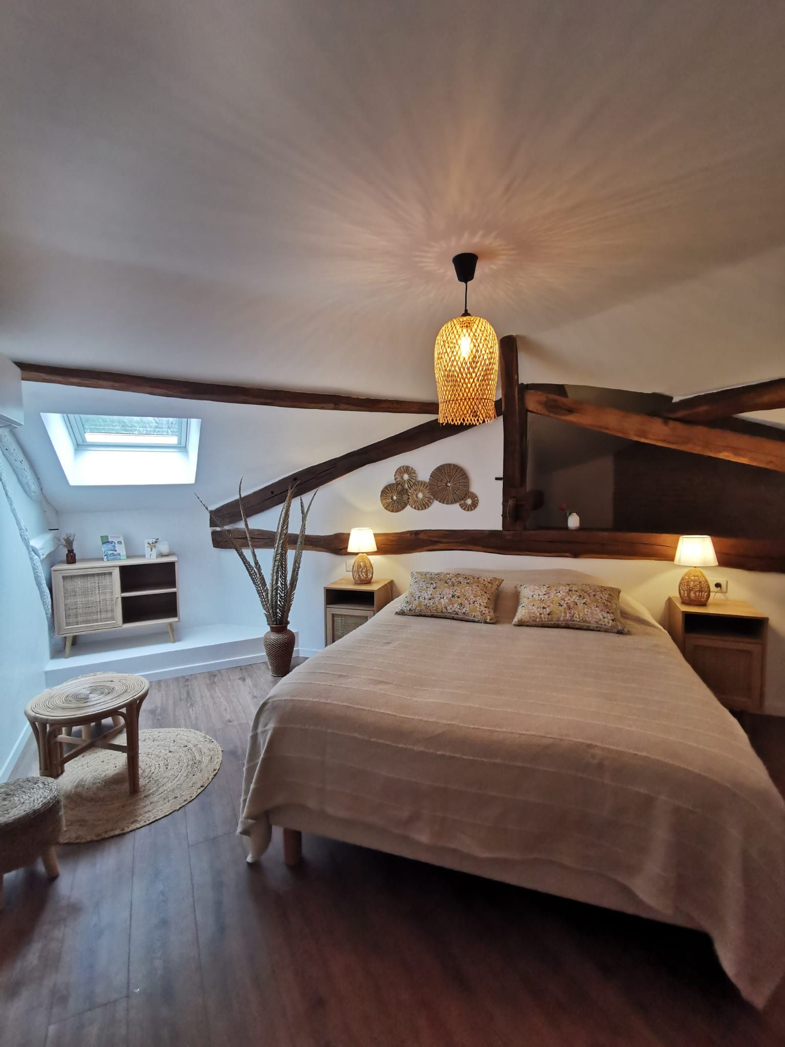 Une chambre avec un plafond en pente, un lit, deux tables de chevet avec des lampes, une petite table ronde et une plante en pot.