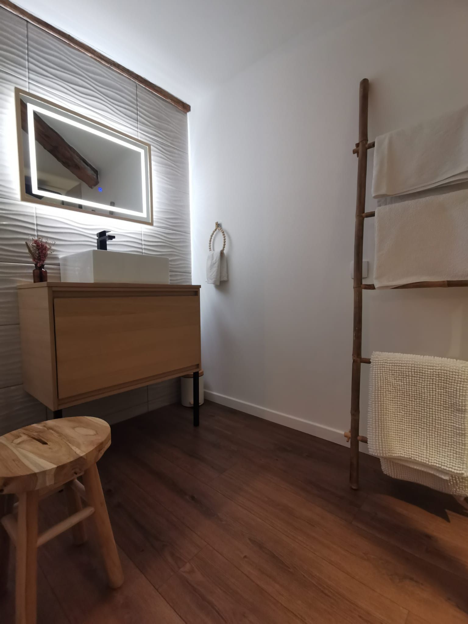 Un baño con tocador de madera, un espejo, un perchero y un taburete de madera.