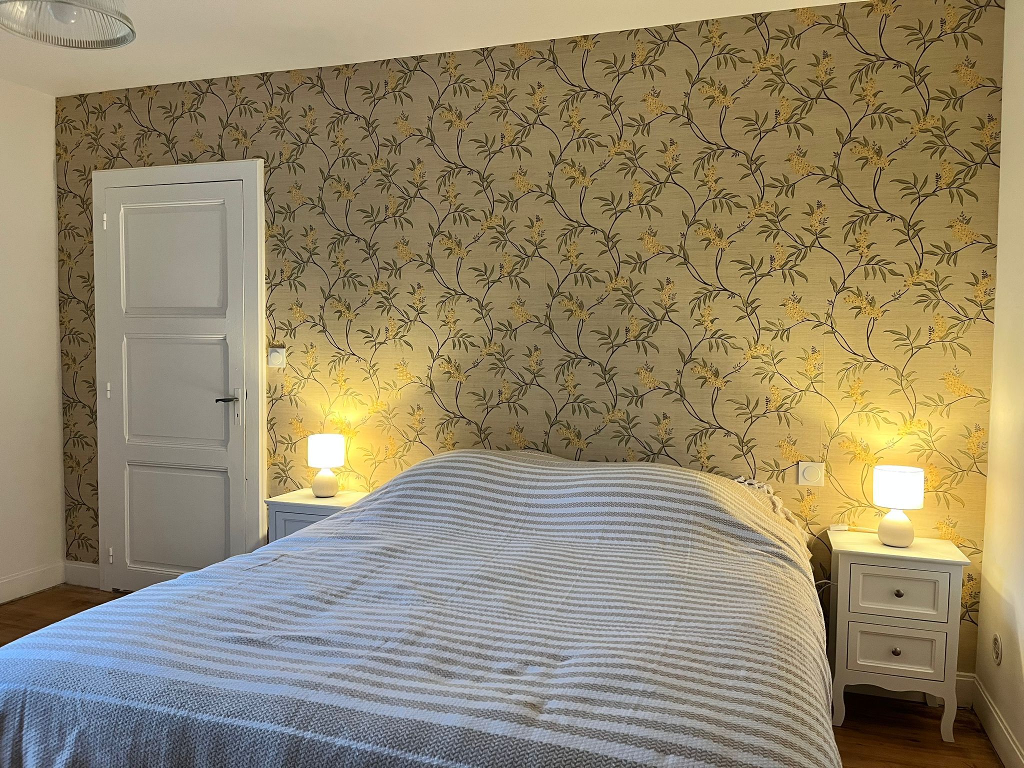 A bedroom with a bed, two bedside tables with lamps, a door, and floral wallpaper.