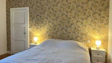 A bedroom with a bed, two bedside tables with lamps, a door, and floral wallpaper.