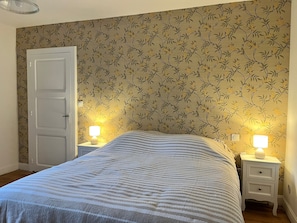 A bedroom with a bed, two bedside tables with lamps, a door, and floral wallpaper.