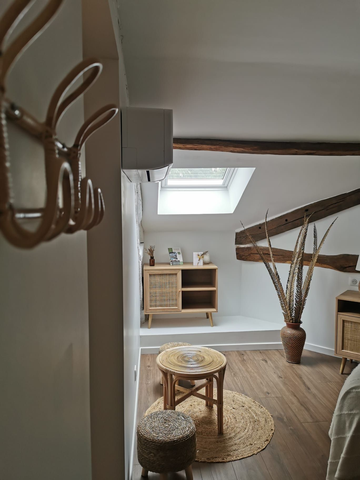 A cozy loft bedroom with a sloped ceiling, a skylight, a wooden bed, a small round table, and a wicker chair.