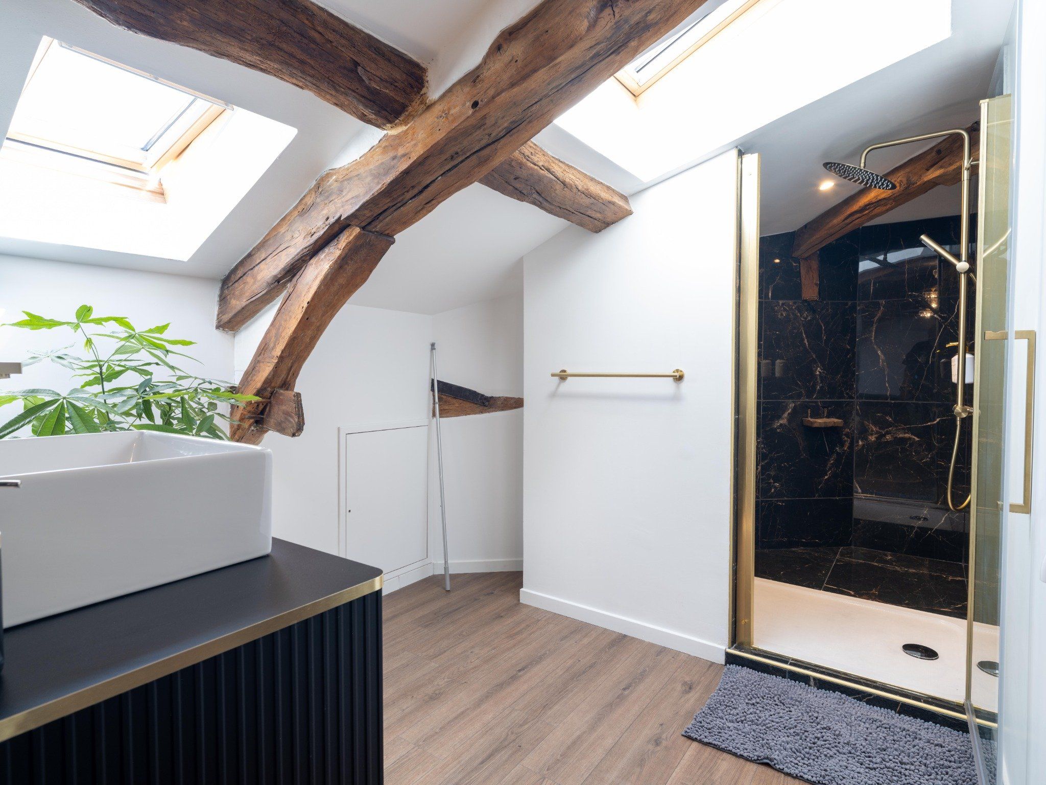 Une salle de bain moderne avec des fenêtres de toit, une douche et une poutre en bois au plafond.
