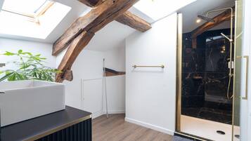 Une salle de bain moderne avec des fenêtres de toit, une douche et une poutre en bois au plafond.