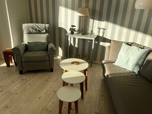 A living room with a sofa, armchair, and a small table with a lamp. - Holiday Apartment in Wyk on Fohr With Balcony (Wyk auf Foehr)