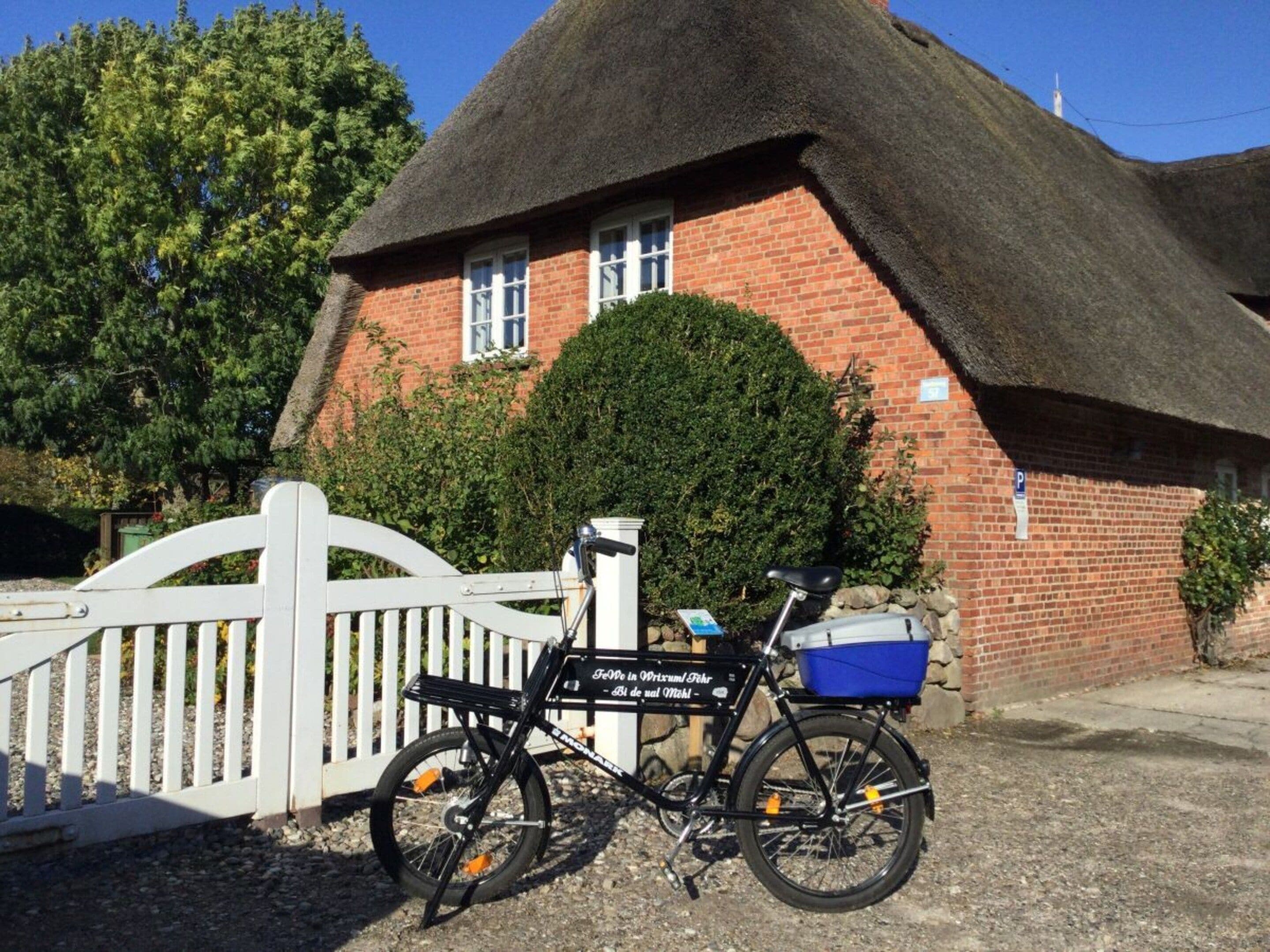 A bicycle parked in front of a thatched-roof house with a white fence.