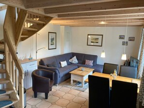 Un salon confortable avec un canapé, une table basse et des fauteuils, un escalier et un coin repas comprenant une table et des chaises.