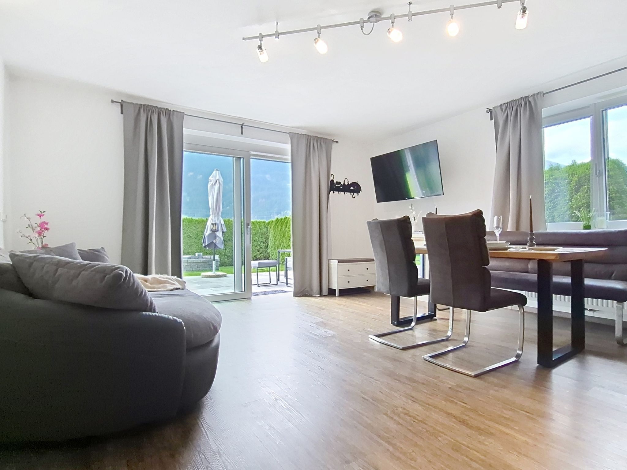 A modern living room with a sofa, dining table, chairs, and a flat-screen TV.