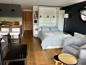 A compact living space with a kitchenette, a bed with a patterned duvet, a grey sofa, and a small round wooden table. - A beautiful houseboat suite with a sauna and jacuzzi (Saint-Cloud)