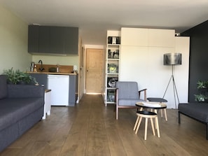 Een moderne woonruimte met een keuken, grijze banken, een kleine ronde tafel en een vloerlamp.
