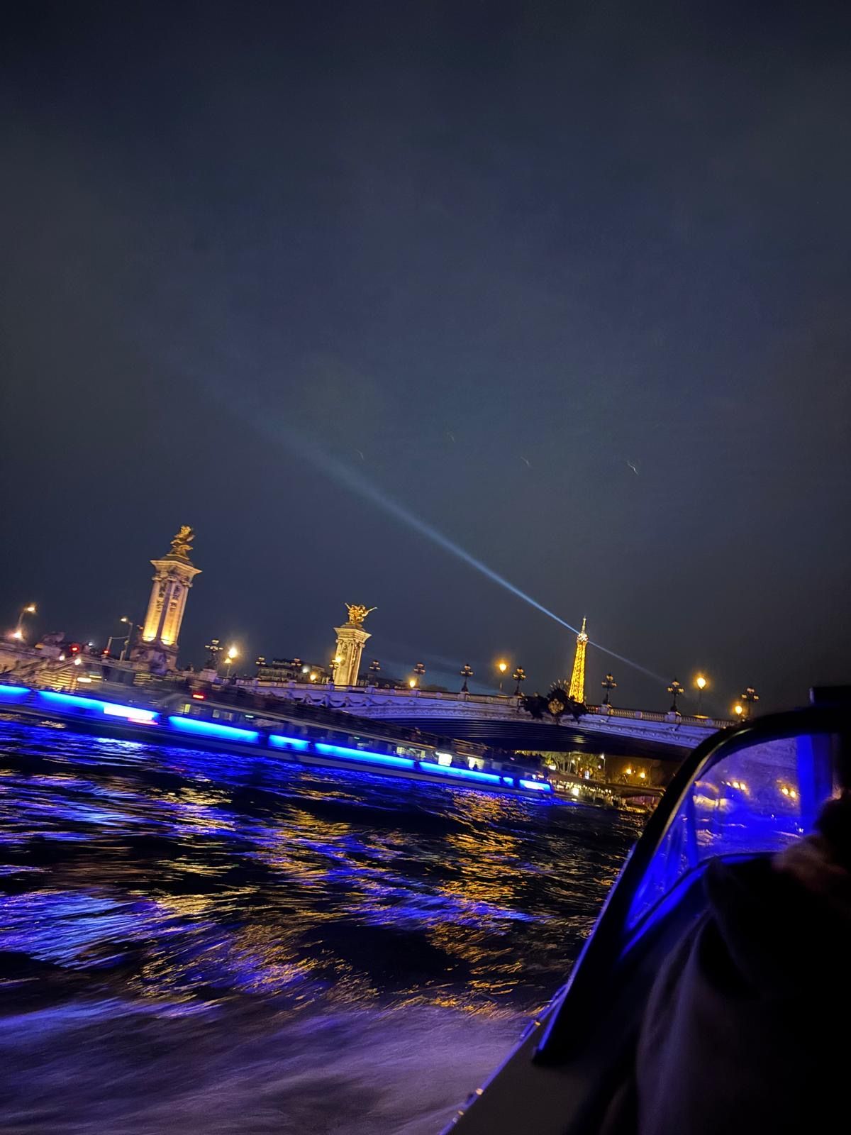 Une vue nocturne d’une rivière, avec des bâtiments illuminés et un pont.