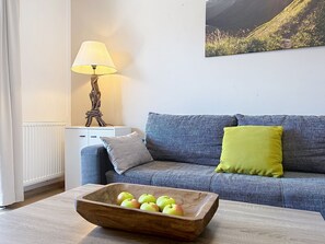 A living room with a sofa, a wooden table with apples, a lamp, and a painting on the wall. - Edelweiss am See by Interhome (Zell am See)