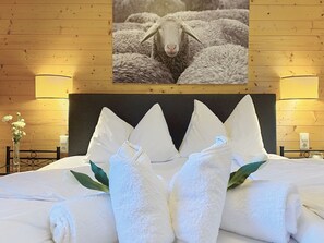 A hotel room with a neatly made bed, white towels, and a framed picture of sheep on the wall. - Edelweiss am See by Interhome (Zell am See)