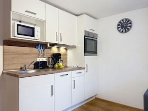 A modern kitchen with white cabinets, a microwave, a kettle, and a clock on the wall. - Hochkönig am See by Interhome (Zell am See)