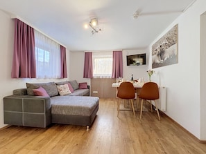 A modern living room with a sofa, a dining table with chairs, a TV mounted on the wall, and a radiator. - Hochkönig am See by Interhome (Zell am See)