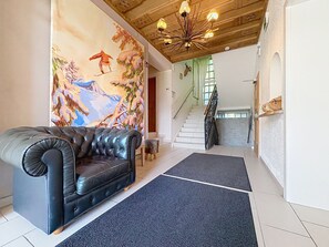A living room with a black leather sofa, a colorful mural, a staircase, and a wooden ceiling. - Schmittenhöhe am See by Interhome (Zell am See)