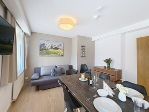 Ein modernes Wohnzimmer mit einer Couch, einem Esstisch und einem an der Wand befestigten Fernseher.