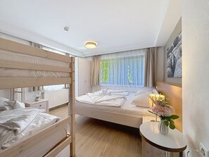 A hotel room with a bunk bed, a single bed, a bedside table with a vase of flowers, and a window with curtains. - Schmittenhöhe am See by Interhome (Zell am See)