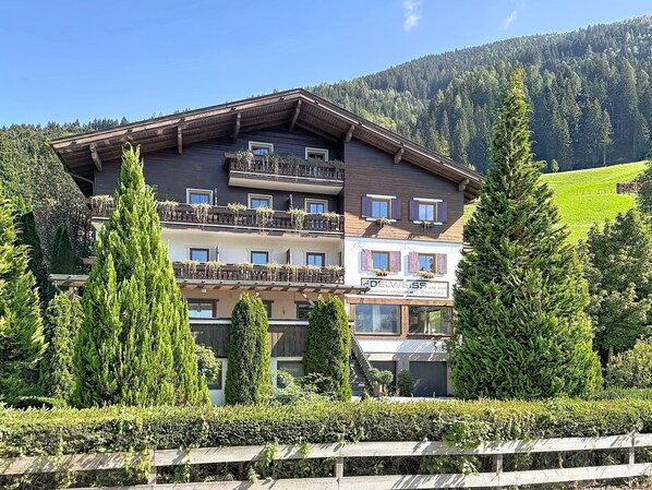 Ein mehrstöckiges Hotel mit Balkonen, umgeben von Grünpflanzen und einer Berglandschaft.
