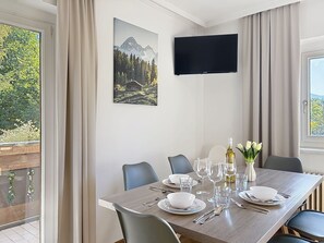A dining room with a table set for four, a flat-screen TV mounted on the wall, and a scenic mountain view through the window. - Imbachhorn am See by Interhome (Zell am See)
