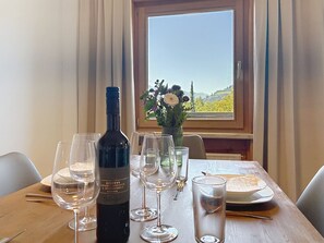 A dining table with a bottle of wine, several glasses, and a vase with flowers. - Schwalbenwand am See by Interhome (Zell am See)