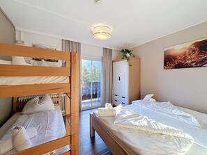 Een hotelkamer met een stapelbed, een enkel bed, een radiator, een kledingkast, een plant en een schilderij aan de muur.