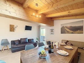 A dining area with a wooden table set for a meal, a sofa, and a television on the wall. - Kitzsteinhorn am See by Interhome (Zell am See)