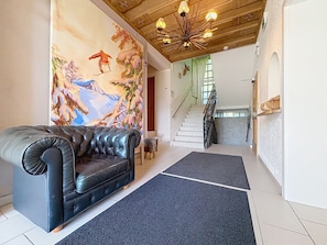 A living room with a black leather sofa, a colorful mural, a staircase, and a wooden ceiling. - Kitzsteinhorn am See by Interhome (Zell am See)
